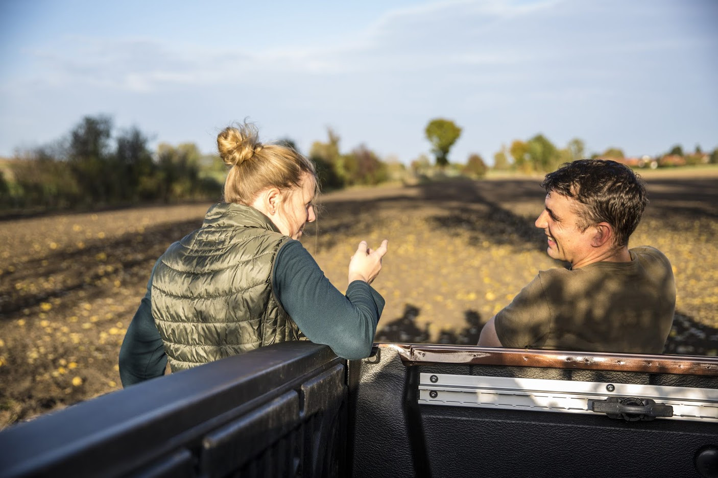 Woman and man sitting on back of truck, chatting.