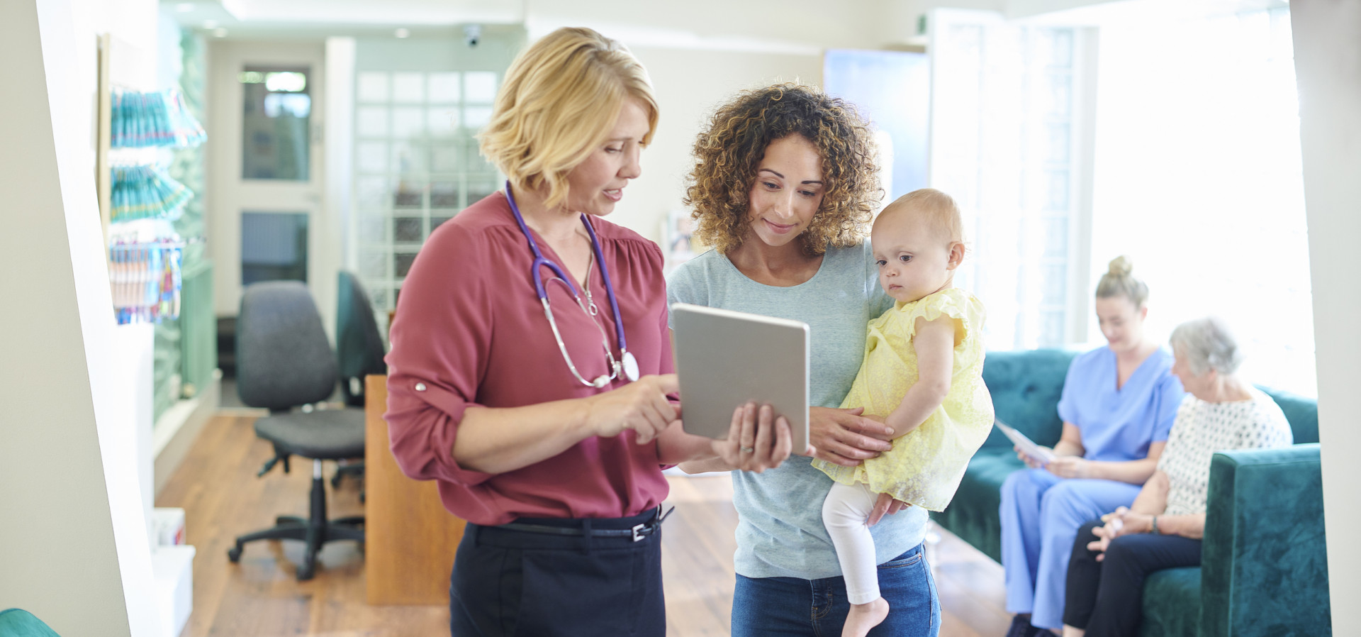 GP speaking with woman and child, showing information on tablet device.